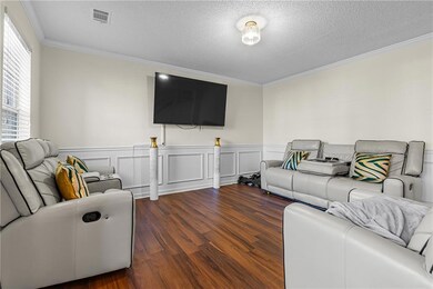 Living area with ornamental molding, a decorative wall, wood finished floors, a wainscoted wall, and a textured ceiling