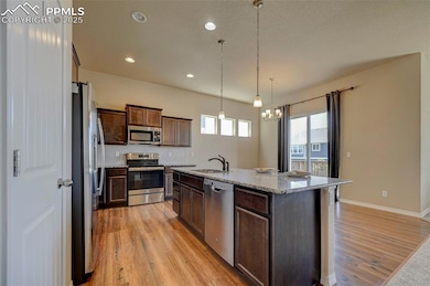 Kitchen featuring dark brown cabinetry, appliances with stainless steel finishes, light stone countertops, a sink, and light wood finished floors