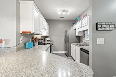Kitchen with light countertops, appliances with stainless steel finishes, white cabinetry, a textured ceiling, and light wood finished floors
