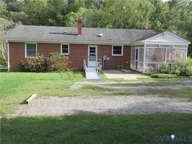 Back of property featuring a chimney, brick siding, roof with shingles, a yard, and a sunroom