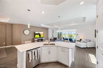 Kitchen featuring a tray ceiling, a center island with sink, dishwasher, white cabinetry, and open floor plan