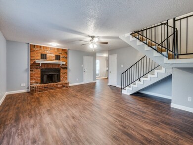 Unfurnished living room featuring a textured ceiling, a brick fireplace, stairs, dark wood-style flooring, and a ceiling fan