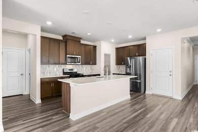 Kitchen featuring decorative backsplash, a center island with sink, stainless steel appliances, dark brown cabinetry, and recessed lighting