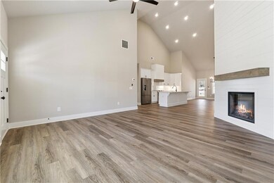 Unfurnished living room with high vaulted ceiling, a ceiling fan, a fireplace, wood finished floors, and a sink