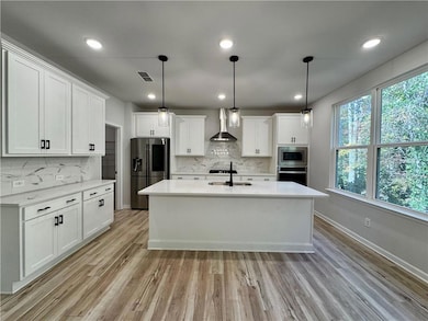 Kitchen featuring decorative light fixtures, white cabinetry, stainless steel appliances, light stone counters, and light wood-style floors