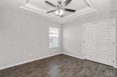 Unfurnished bedroom with a tray ceiling, dark wood-style floors, a closet, baseboards, and a ceiling fan