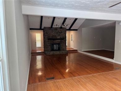 Unfurnished living room with wood finished floors, a textured ceiling, a stone fireplace, and ceiling fan