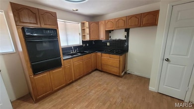 Kitchen featuring dark countertops, backsplash, black appliances, light wood finished floors, and a warming drawer