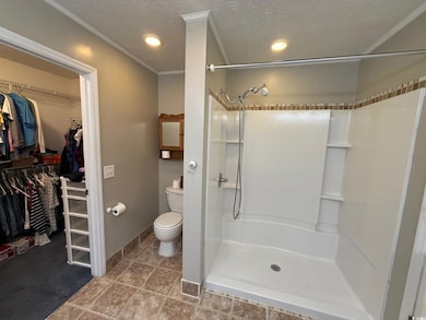 Bathroom featuring a stall shower, ornamental molding, toilet, a spacious closet, and a textured ceiling