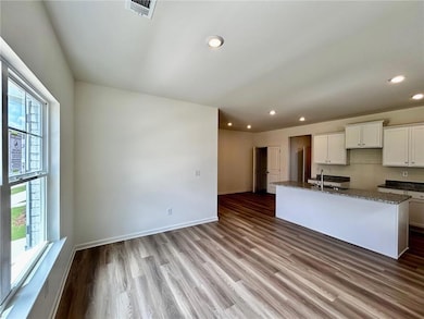 Kitchen featuring dark stone countertops, recessed lighting, white cabinets, wood finished floors, and a center island with sink
