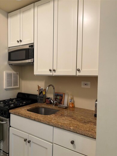Kitchen with stainless steel range, white cabinetry, dark stone countertops, and white microwave