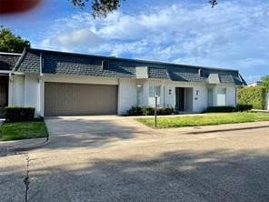 View of front facade with concrete driveway, mansard roof, and an attached garage