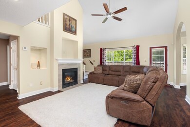 Living room with ceiling fan, wood finished floors, high vaulted ceiling, a tiled fireplace, and baseboards