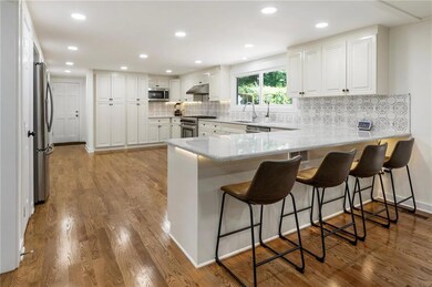 Kitchen with appliances with stainless steel finishes, a peninsula, under cabinet range hood, wood finished floors, and recessed lighting