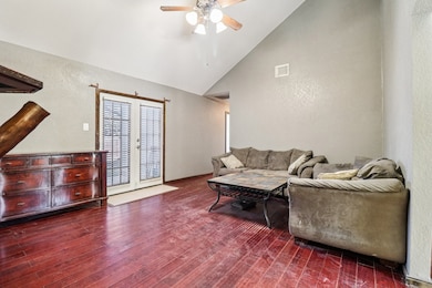 Living area featuring a textured wall, high vaulted ceiling, dark wood-style floors, a ceiling fan, and french doors