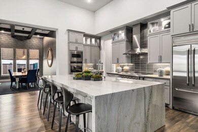 A chef's dream kitchen awaits in this open-concept masterpiece. Featuring sleek, light gray cabinetry and a stunning, oversized kitchen island with a cascading waterfall edge in gorgeous quartzite. The gourmet space is appointed with top-of-the-line stainless steel appliances, a stylish tile backsplash, and designer lighting throughout. The seamless flow into the sophisticated dining area, accented by a striking wallpaper and contemporary lighting, makes this the ultimate space for entertaining.