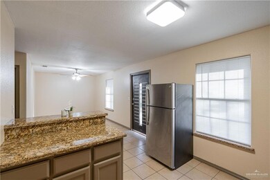 Kitchen with freestanding refrigerator, light stone counters, light tile patterned floors, a ceiling fan, and a textured ceiling