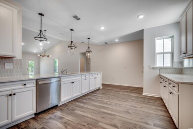 Kitchen with stainless steel dishwasher, backsplash, a sink, lofted ceiling, and light countertops