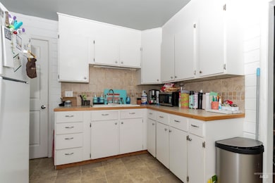 Kitchen featuring freestanding refrigerator, white cabinets, and decorative backsplash