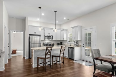 Kitchen featuring decorative light fixtures, stainless steel appliances, a breakfast bar area, white cabinets, and a center island