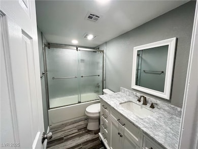 Bathroom featuring combined bath / shower with glass door, vanity, dark wood finished floors, and a textured wall