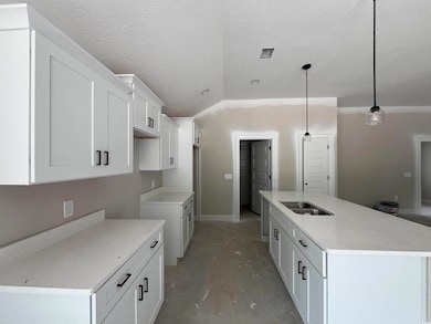 Kitchen featuring vaulted ceiling, a kitchen island with sink, white cabinets, concrete floors, and a textured ceiling