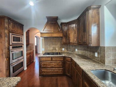 Kitchen with tasteful backsplash, light stone countertops, appliances with stainless steel finishes, custom exhaust hood, and dark wood-type flooring