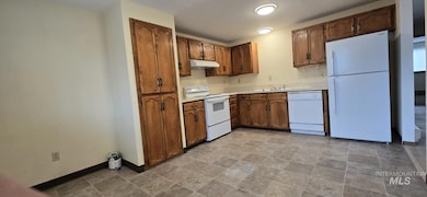 Kitchen with white appliances, light countertops, stone finish flooring, brown cabinetry, and under cabinet range hood