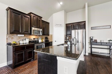 Kitchen with backsplash, stainless steel appliances, dark brown cabinets, sink, and dark stone counters
