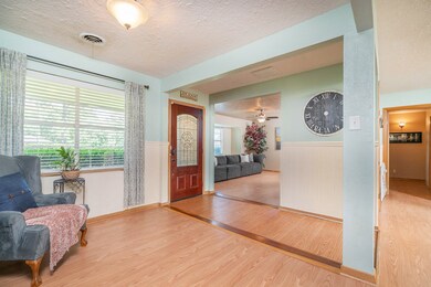 Step through a solid mahogany front door with a Texas themed leaded glass detailed inset into an inviting foyer with durable wood look laminate floors, charming beadboard panels, and soft pastel paint throughout the adjoining living spaces.
