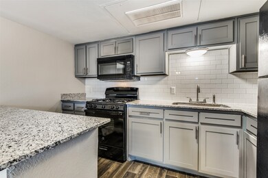 Kitchen with gray cabinets, black appliances, light stone counters, and dark wood finished floors