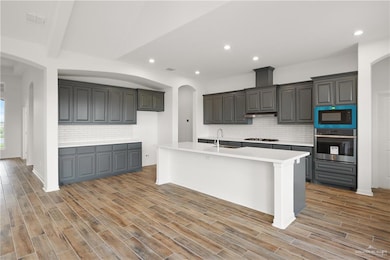 Kitchen featuring stainless steel appliances, a sink, tasteful backsplash, light countertops, and an island with sink