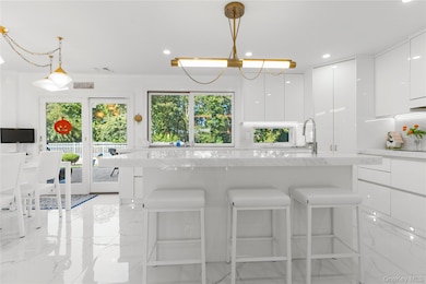 Kitchen featuring modern cabinets, a kitchen bar, white cabinetry, light stone counters, and recessed lighting