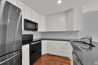 Kitchen featuring black appliances, light wood-type flooring, dark stone counters, white cabinetry, and recessed lighting