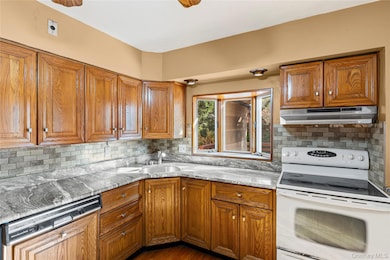 Kitchen featuring white range with electric cooktop, brown cabinetry, dishwasher, and backsplash