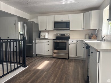 Kitchen featuring stainless steel appliances, a sink, dark wood-style floors, light countertops, and a textured ceiling