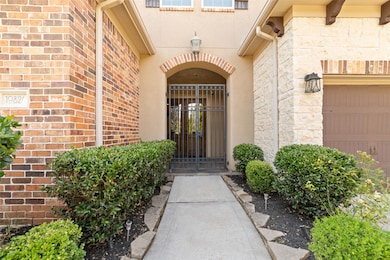 The entrance features a gated archway, bordered by well-maintained shrubs. The exterior is a combination of brick and stone with a welcoming walkway leading to the front door.