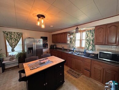 Kitchen with stainless steel appliances, light flooring, a kitchen island, dark countertops, and brown cabinetry