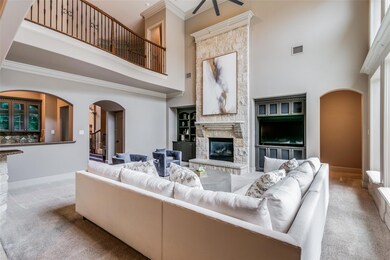 Carpeted living room with built in shelves, a stone fireplace, crown molding, and a high ceiling