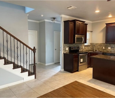 Kitchen with dark brown cabinetry, stainless steel appliances, light tile patterned floors, crown molding, and dark stone countertops