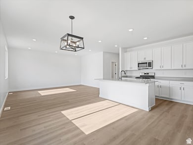 Kitchen featuring white cabinets, an island with sink, a chandelier, stainless steel appliances, and light wood finished floors