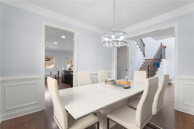 Dining space featuring a chandelier, dark wood-style flooring, a wainscoted wall, stairs, and a decorative wall