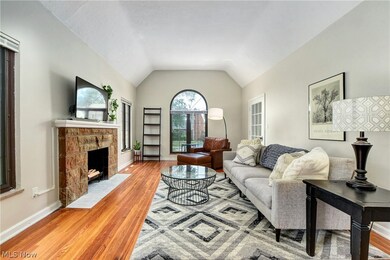Living room with hardwood floors, a stone surround fireplace, and vaulted ceiling