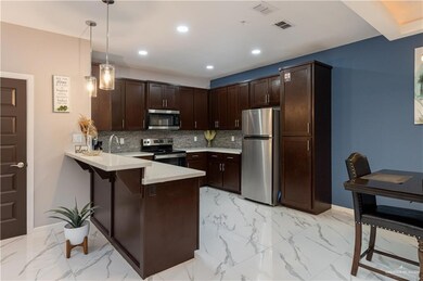 Kitchen featuring light tile flooring, dark brown cabinets, appliances with stainless steel finishes, pendant lighting, and tasteful backsplash