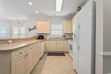 Kitchen featuring white appliances, crown molding, recessed lighting, light tile patterned floors, and a peninsula