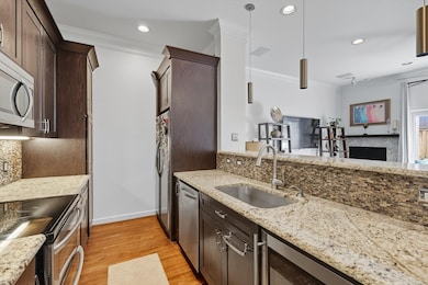 Kitchen with light stone counters, hanging light fixtures, stainless steel appliances, dark brown cabinetry, and ornamental molding