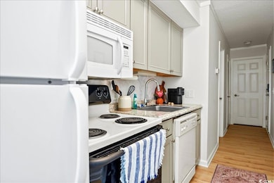 Kitchen featuring white appliances, light wood-style floors, light countertops, a textured ceiling, and tasteful backsplash