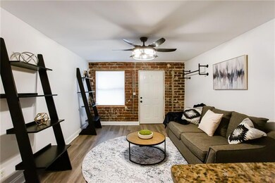 Living room featuring brick wall, ceiling fan, wood finished floors, and baseboards