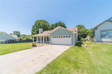 Ranch-style home featuring an attached garage, a chimney, driveway, and covered porch