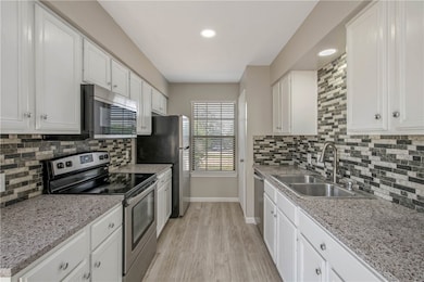Kitchen with tasteful backsplash, stainless steel appliances, white cabinets, and recessed lighting